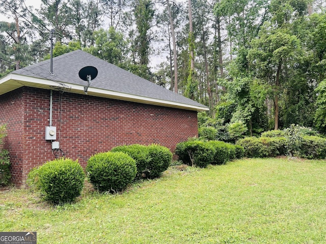 view of side of property with a yard, brick siding, roof with shingles, and view of scattered trees