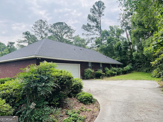 view of side of property featuring brick siding, an attached garage, driveway, and roof with shingles