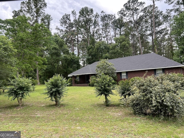 view of side of property featuring a yard, roof with shingles, and view of wooded area