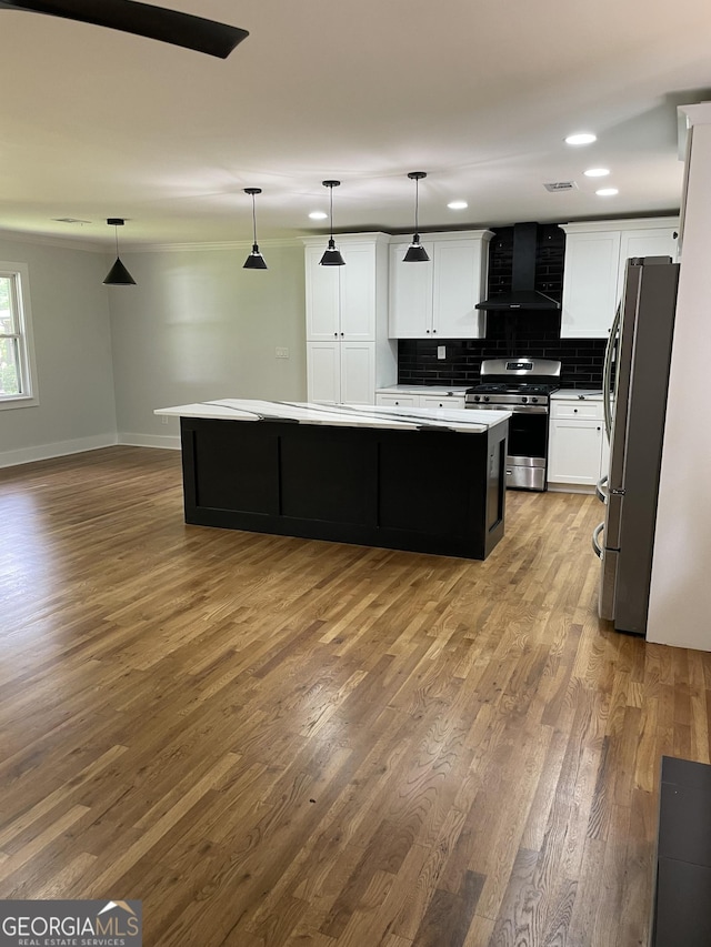 kitchen featuring appliances with stainless steel finishes, wall chimney range hood, a kitchen island, wood finished floors, and decorative backsplash