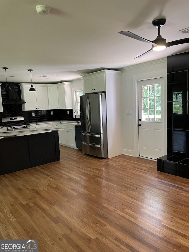 kitchen with appliances with stainless steel finishes, ceiling fan, wall chimney range hood, backsplash, and dark wood-style flooring