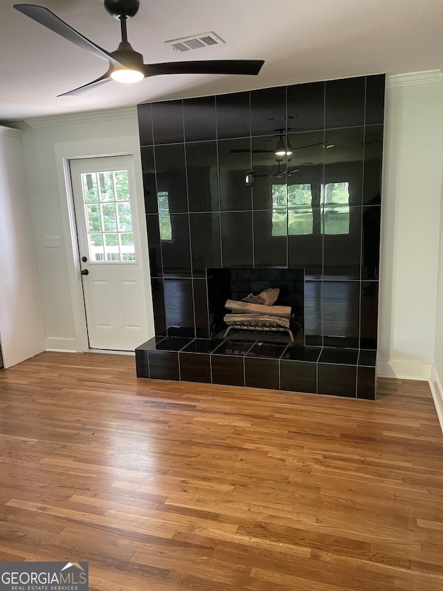 bathroom featuring ornamental molding, wood finished floors, a ceiling fan, a tiled fireplace, and baseboards