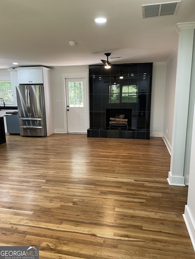 unfurnished living room with wood finished floors, baseboards, ornamental molding, recessed lighting, and a tiled fireplace