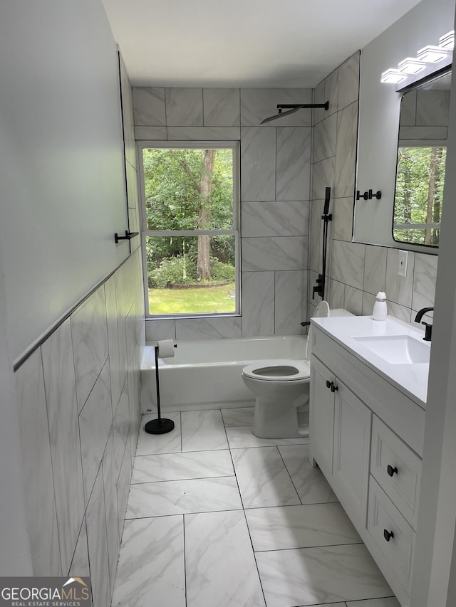 bathroom featuring tile walls, marble look tile flooring, toilet, vanity, and tub / shower combination