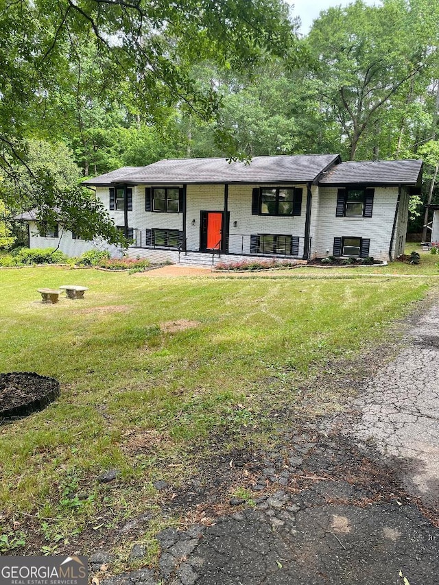 raised ranch featuring covered porch, a front yard, and brick siding
