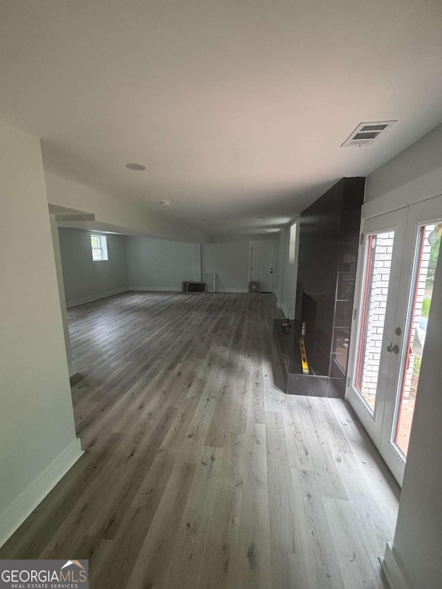 unfurnished living room featuring wood finished floors, baseboards, plenty of natural light, and french doors