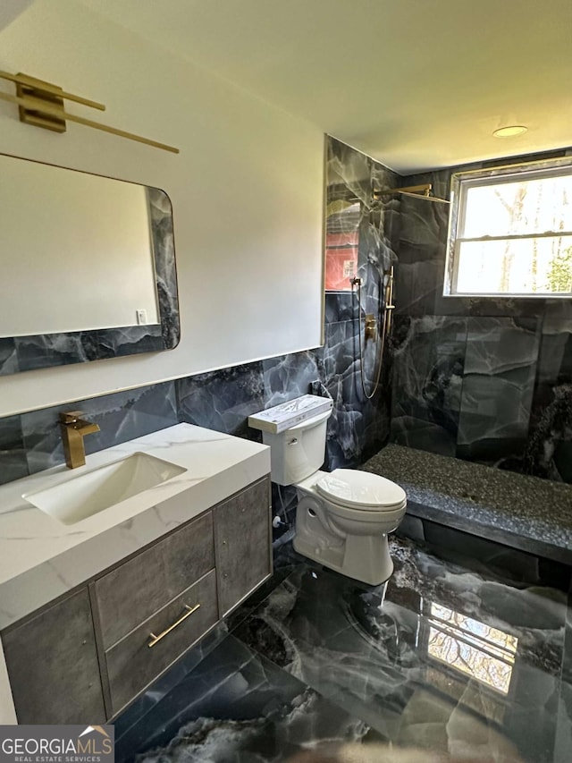 full bath featuring tile walls, marble tiled floors, toilet, a walk in shower, and vanity