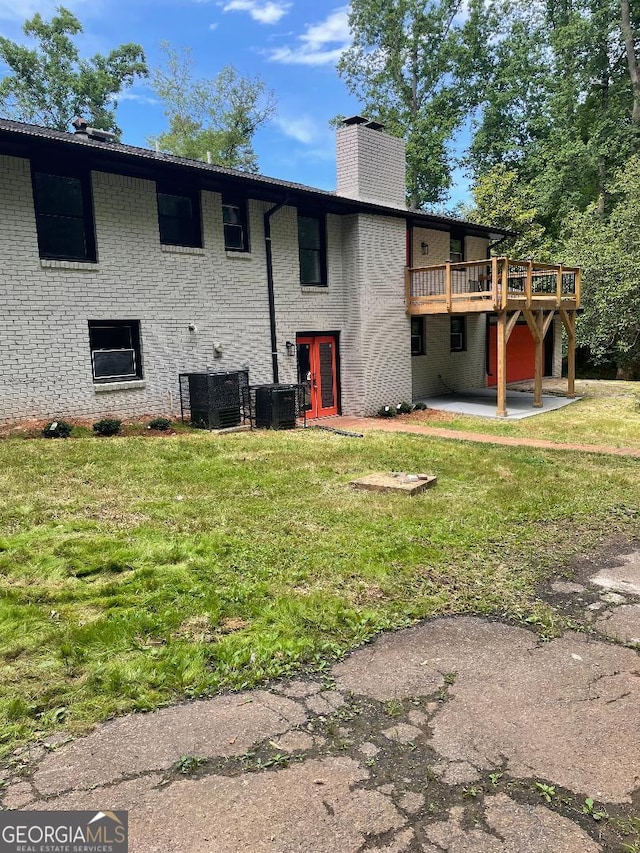 rear view of property featuring a deck, a chimney, a patio, a lawn, and brick siding