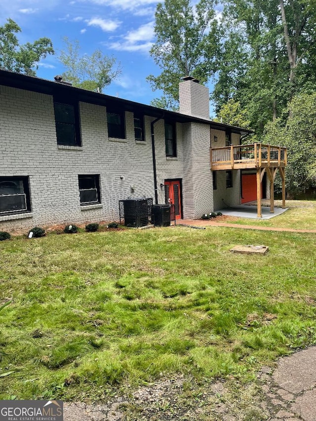 rear view of house featuring a deck, a chimney, a lawn, brick siding, and central air condition unit