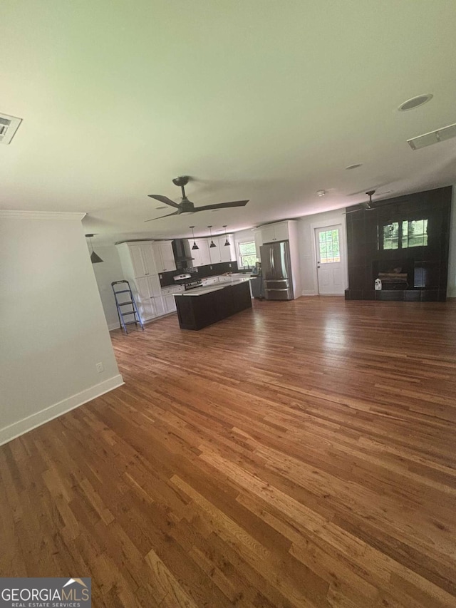 unfurnished living room with dark wood-type flooring, baseboards, a ceiling fan, and ornamental molding