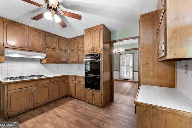 kitchen with stainless steel gas cooktop, under cabinet range hood, brown cabinets, and light wood finished floors