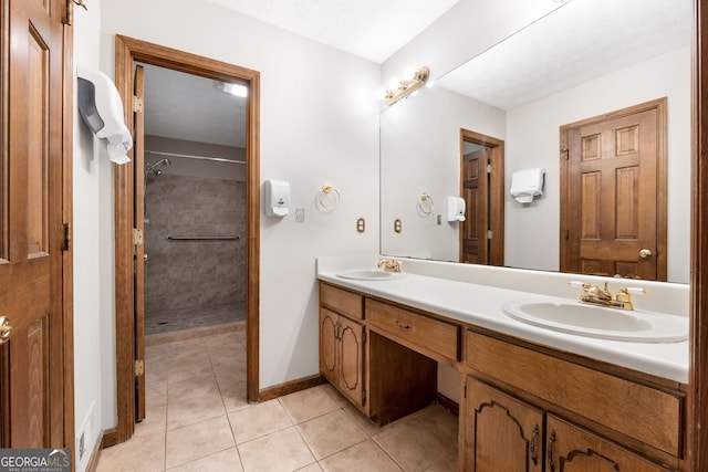 bathroom with tile patterned floors, double vanity, tiled shower, and baseboards