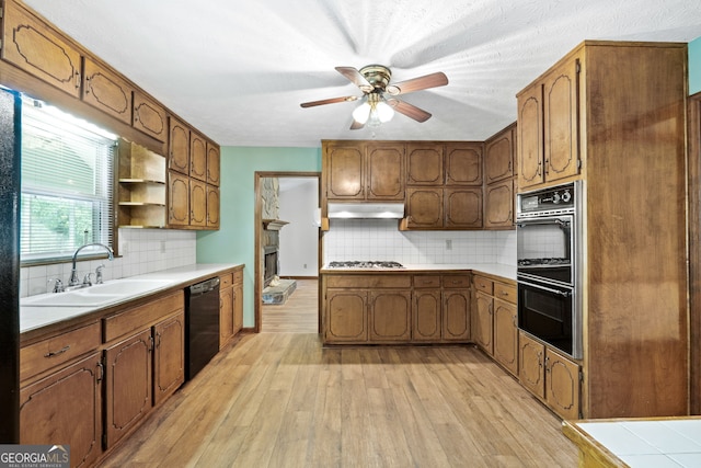 kitchen with black dishwasher, a sink, multiple ovens, a ceiling fan, and stainless steel gas cooktop