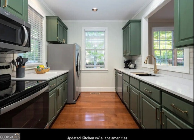 kitchen featuring stainless steel appliances, green cabinetry, a sink, crown molding, and recessed lighting