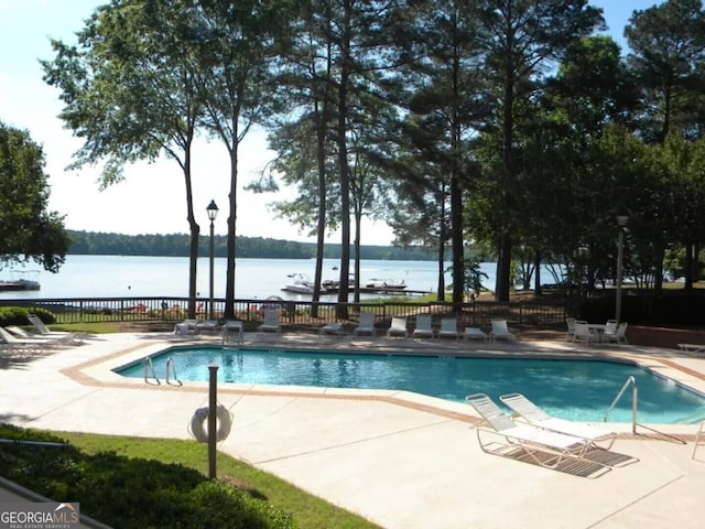 community pool with a patio, a water view, and fence