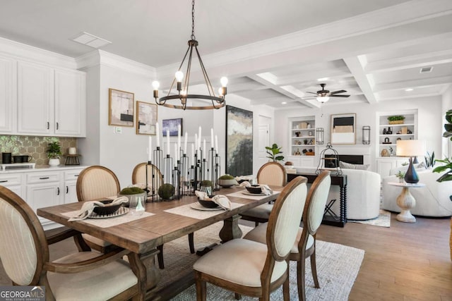 dining space featuring light wood finished floors, beamed ceiling, a chandelier, ceiling fan, and built in features
