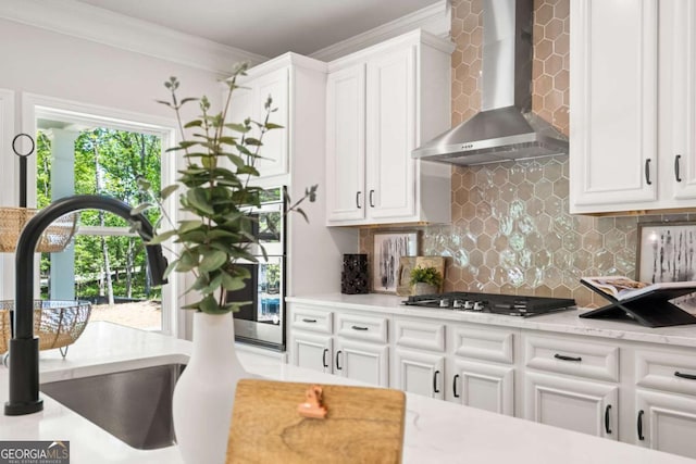 kitchen with wall chimney exhaust hood, stainless steel gas cooktop, a sink, crown molding, and white cabinetry