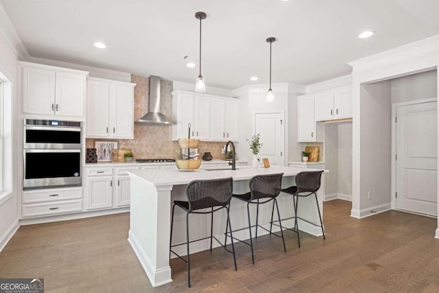 kitchen with wall chimney range hood, stainless steel appliances, white cabinets, a sink, and tasteful backsplash