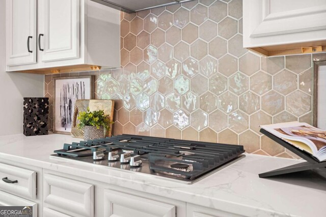 kitchen view of stainless steel gas cooktop, backsplash, white cabinets, and light stone counters