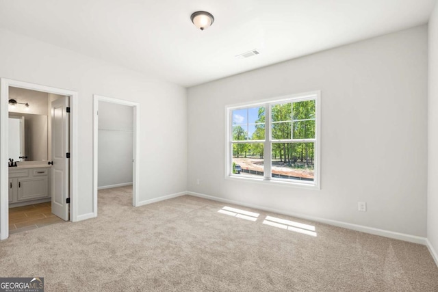 unfurnished bedroom featuring light colored carpet, a walk in closet, baseboards, and ensuite bathroom
