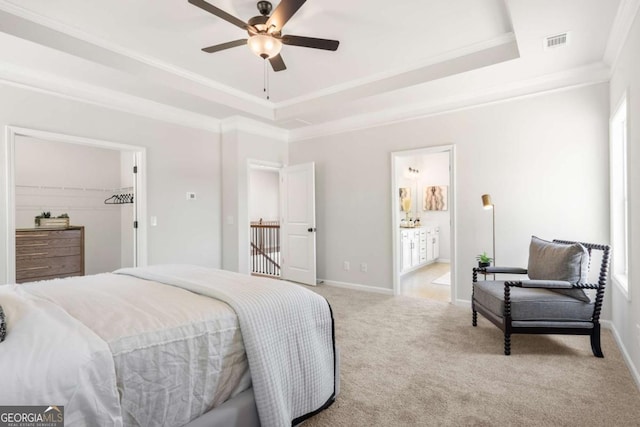 bedroom featuring a tray ceiling, light carpet, crown molding, baseboards, and connected bathroom