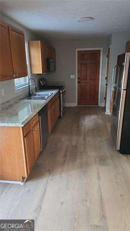 kitchen with appliances with stainless steel finishes, a sink, light wood finished floors, baseboards, and brown cabinets