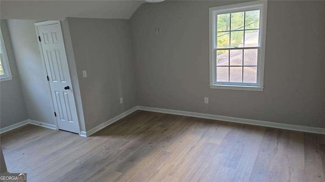 unfurnished room with plenty of natural light, wood finished floors, baseboards, and lofted ceiling