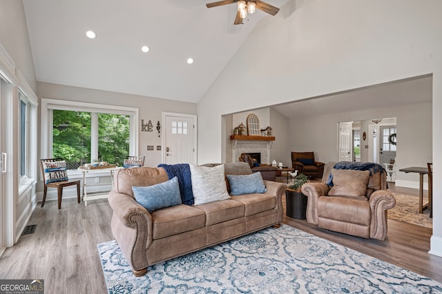living room with high vaulted ceiling, light wood-type flooring, recessed lighting, a fireplace, and a ceiling fan