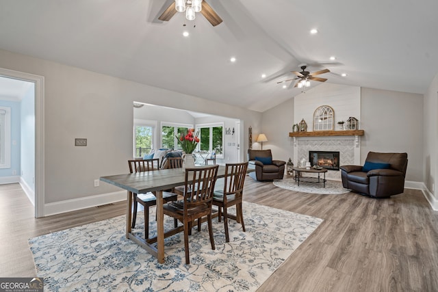 dining area with a ceiling fan, wood finished floors, baseboards, vaulted ceiling, and a tile fireplace