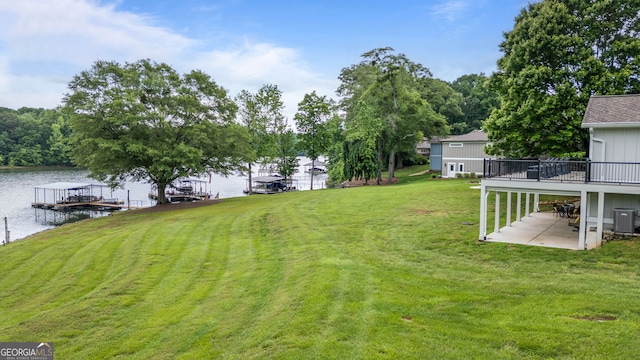 view of grassy yard with a patio, central AC unit, a boat dock, and a deck with water view