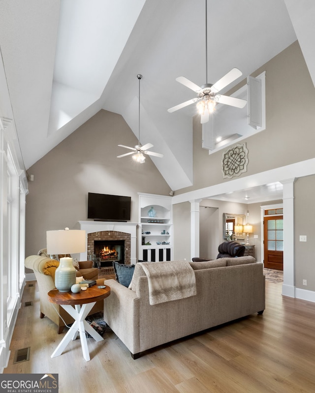 130 Allie Dr, Mcdonough, GA 30252 - living area with decorative columns, high vaulted ceiling, a ceiling fan, a brick fireplace, and light wood-style floors