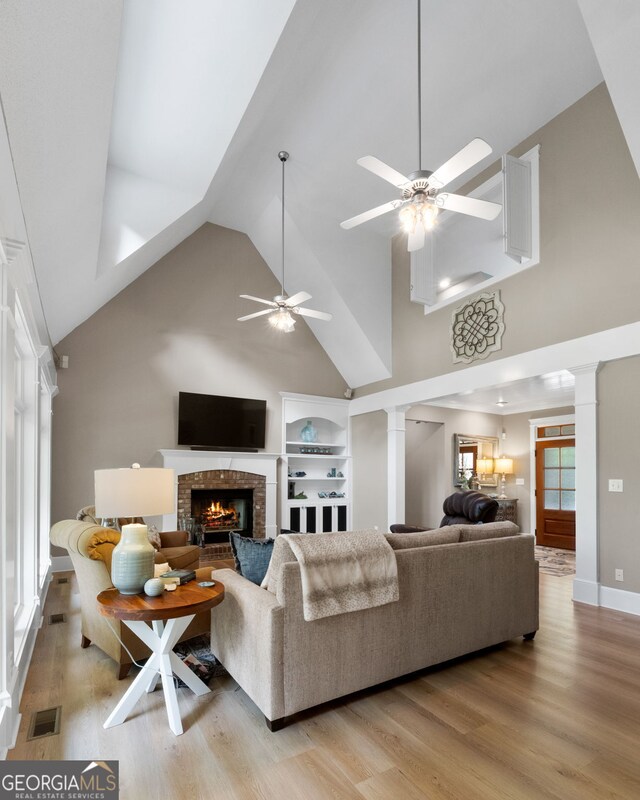 130 Allie Dr, Mcdonough, GA 30252 - living area with decorative columns, high vaulted ceiling, a ceiling fan, a brick fireplace, and light wood-style floors