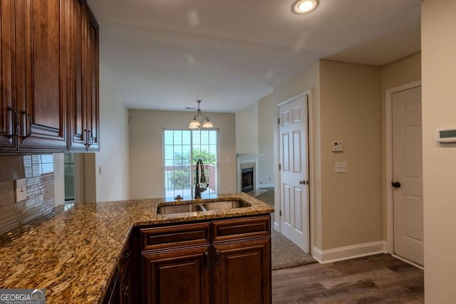 kitchen with a sink, a peninsula, dark wood finished floors, a fireplace, and stone countertops