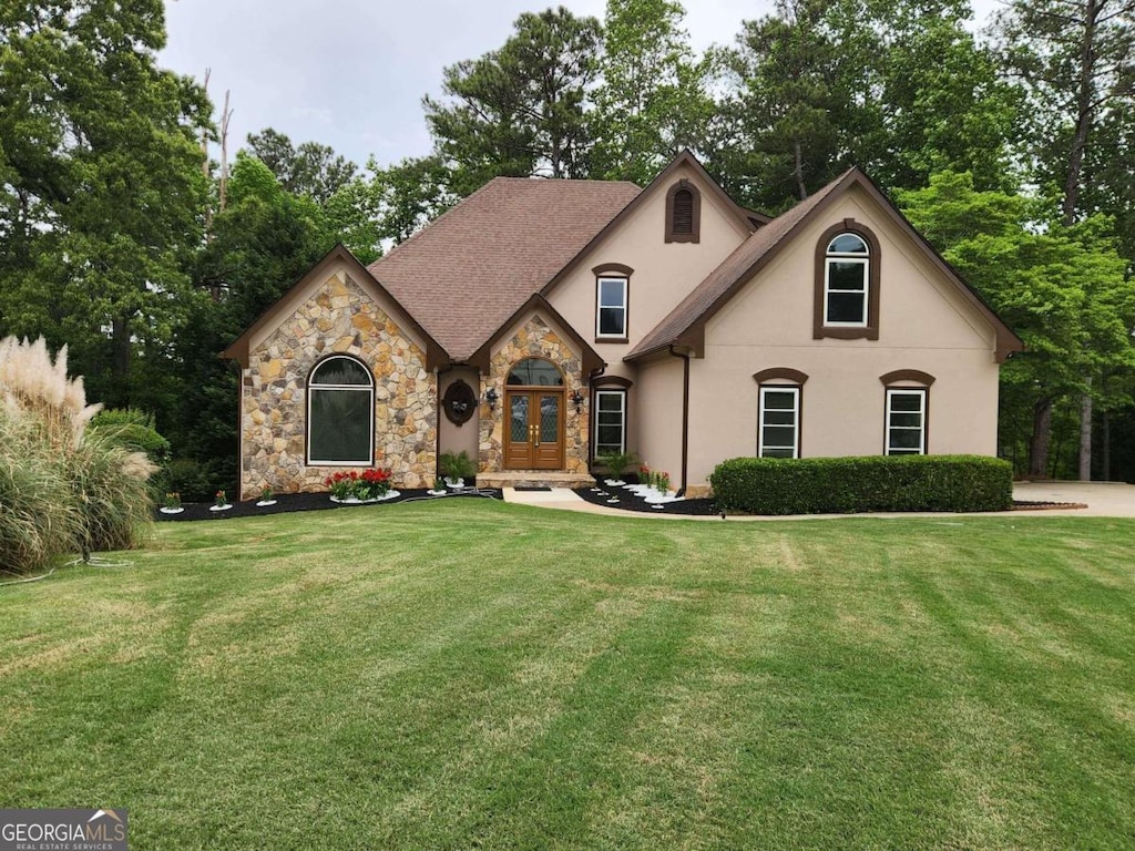 french country home featuring french doors, a front yard, stone siding, and stucco siding