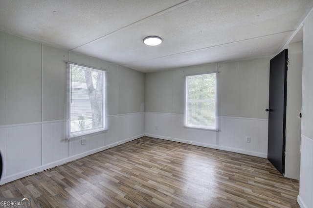 unfurnished room with wood finished floors, a textured ceiling, wainscoting, and a decorative wall