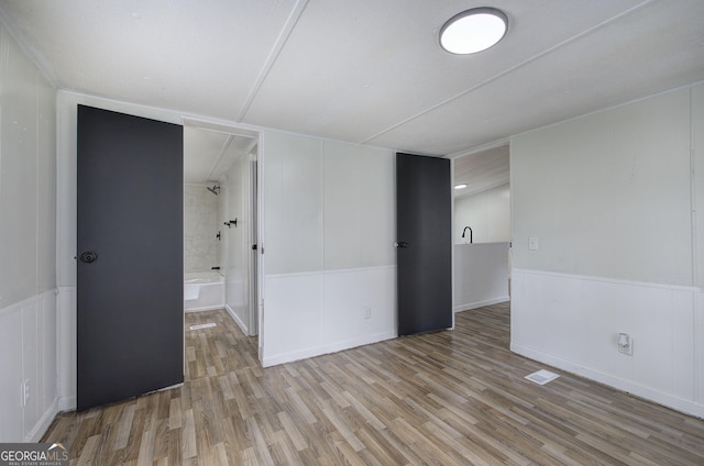 unfurnished bedroom featuring wood finished floors, a decorative wall, and connected bathroom