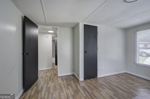 unfurnished room with light wood finished floors, a textured ceiling, and baseboards