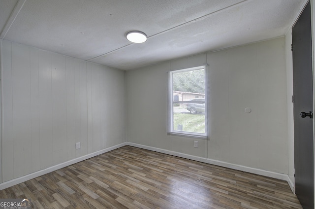 spare room featuring wood finished floors, a textured ceiling, and baseboards