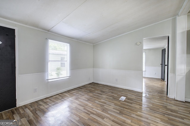 spare room with wood finished floors, crown molding, a wainscoted wall, and lofted ceiling