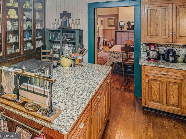 3021 Teamon Rd, Griffin, GA 30223 - kitchen featuring wallpapered walls, dark wood-style floors, brown cabinets, light stone countertops, and glass insert cabinets