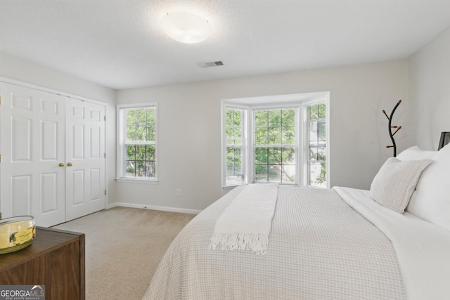 bedroom with multiple windows, light carpet, a closet, and baseboards