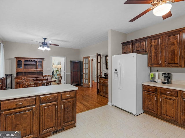 kitchen with white fridge with ice dispenser, a ceiling fan, light countertops, and dark brown cabinets