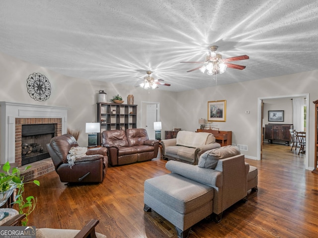 living area with wood finished floors, a fireplace, a ceiling fan, and a textured ceiling