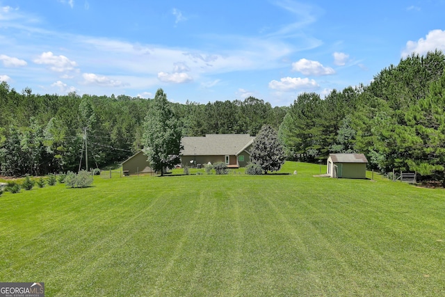 view of grassy yard with a storage shed, an outbuilding, and a view of trees