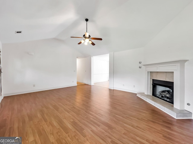 unfurnished living room featuring ceiling fan, light wood-type flooring, vaulted ceiling, a tile fireplace, and baseboards