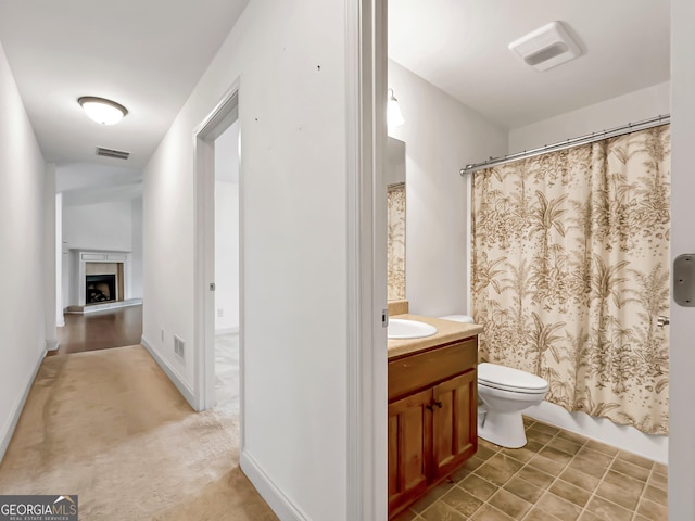 bathroom with toilet, vanity, and a fireplace with raised hearth
