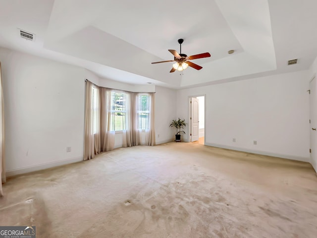 spare room with a raised ceiling, a ceiling fan, light carpet, and baseboards