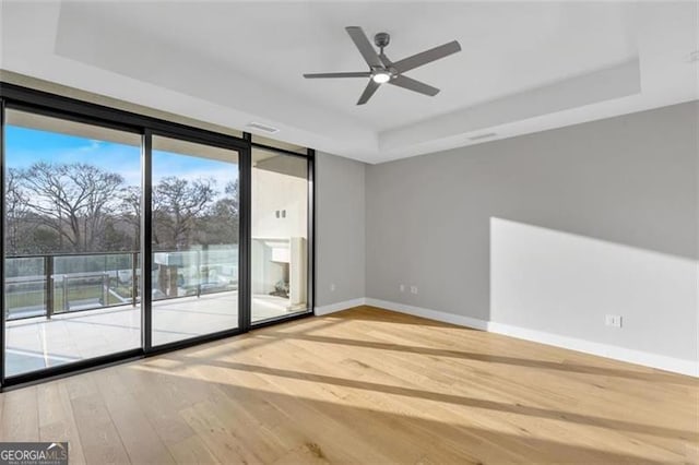unfurnished room with hardwood / wood-style flooring, a tray ceiling, floor to ceiling windows, baseboards, and a ceiling fan