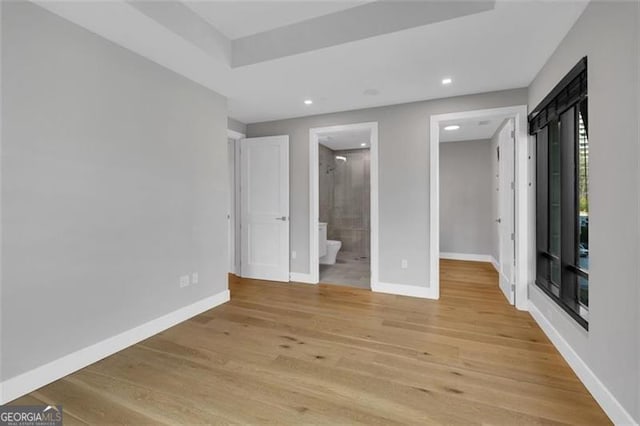 unfurnished bedroom featuring light wood-style floors, baseboards, a walk in closet, recessed lighting, and ensuite bathroom