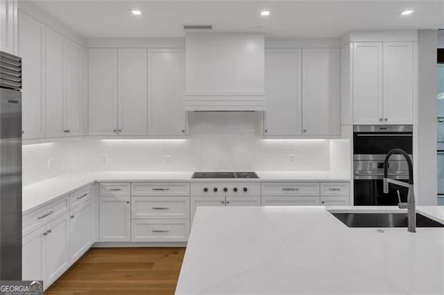 kitchen featuring a sink, custom range hood, white cabinets, appliances with stainless steel finishes, and light wood finished floors